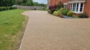 Buff resin bound driveway curving past a lawn to a brick house