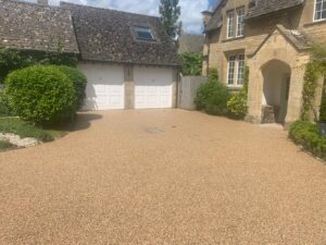 Resin bound driveway in front of a Cotswold stone house and double garage