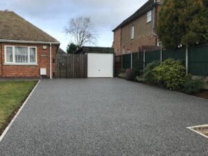 Grey resin bound driveway leading to a garage between two houses